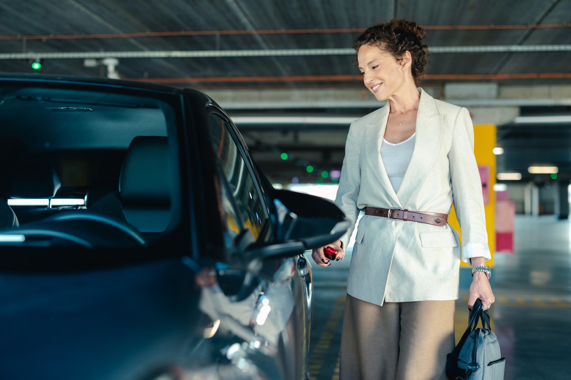 Smiling middle aged business woman opening car door in parking garage